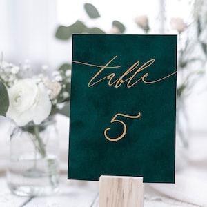May include: A dark green table number card with gold lettering. The card says "table 5" and is on a wooden stand.