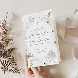 Puede incluir: Una invitación de boda con un diseño floral blanco y un hexágono azul con el texto "The Nuptial Mass Celebrating the Union of Gloria Pauline Gamma and Scott Dennis Teck" y la fecha "Saturday, April 22, 20XX" y la ubicación "St. Mary's Church Portland, Oregon".