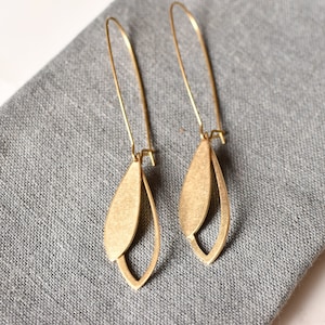 May include: A pair of gold-toned earrings with a leaf-shaped design. The earrings are made of two overlapping pieces of metal, creating a delicate and modern look.