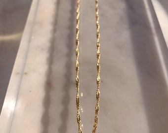 Puede incluir: Un collar de cadena de oro con un diseño delicado y trenzado. La cadena está sobre una superficie de mármol blanco.