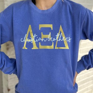 May include: A blue sweatshirt with gold lettering that reads "AEA Christian Brothers". The sweatshirt has long sleeves and a crew neck. The text is in a bold, sans-serif font.
