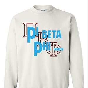 May include: A white crewneck sweatshirt featuring the Greek letters Pi, Beta, and Phi in a layered design. The letters are in a combination of light blue and maroon. The text "EST. 1867" is also visible.