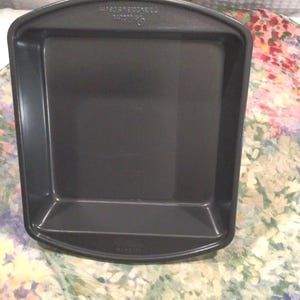 May include: A dark gray square baking pan with slightly rounded edges. The pan has a non-stick surface and is designed for baking. The pan measures 8 inches by 8 inches.