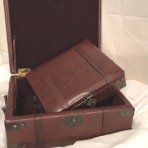 May include: A brown leather-look box with a hinged lid and brass accents. The box is open and the lid is propped up, revealing a brown velvet interior.