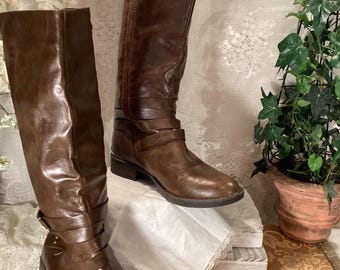 May include: A pair of brown leather knee-high boots with a buckle strap detail and a side zipper closure.