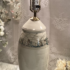 May include: A white ceramic table lamp with a gold base and a light blue and brown floral design. The lamp has a white fabric shade.