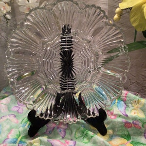 May include: A clear glass serving dish with a scalloped edge and a starburst pattern in the centre. The dish is on a black stand.