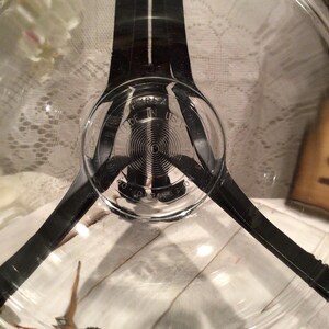 Könnte beinhalten: Eine durchsichtige Glasschüssel mit einem schwarzen Metallrand und drei schwarzen Metallgriffen. Die Schüssel hat ein rundes Etikett mit der Aufschrift "Pyrex Made in USA".