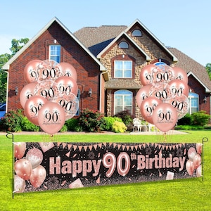 May include: A black banner with gold glitter and the text "Happy 90th Birthday!"  A bunch of rose gold balloons with the number 90 printed on them are in front of a house.