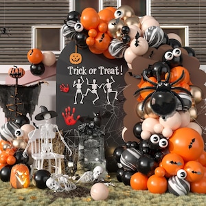 May include: A Halloween party decoration with a black chalkboard sign that says "Trick or Treat!" surrounded by orange, black, and white balloons. There are also two skeletons, a pumpkin, and a spider.