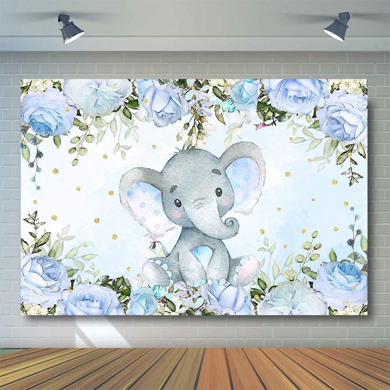 Op de afbeelding: Een lichtblauwe achtergrond met een aquarel-illustratie van een grijze olifant omringd door blauwe rozen en groene bladeren. Goudkleurige glitterpunten zijn over de hele achtergrond verspreid.