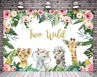 May include: A white backdrop with the text "Two Wild" in gold glitter. The backdrop is decorated with pink and green floral arrangements and features illustrations of a lion, elephant, and giraffe wearing floral crowns.