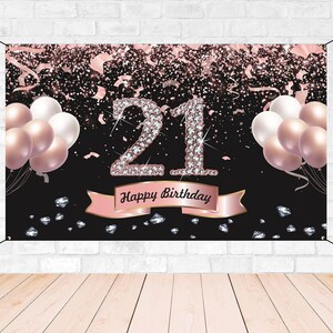 May include: Black and rose gold birthday banner with the number 21 in large, sparkly diamonds. The banner also has the words "Happy Birthday" in a gold ribbon with rose gold accents. The banner is decorated with confetti and balloons.