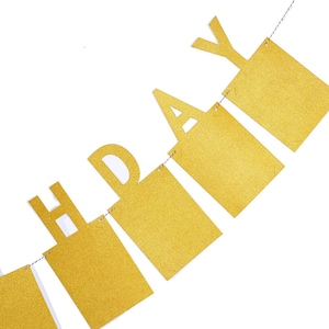 May include: Gold glitter Happy Birthday banner with each letter on a separate piece of cardstock. The banner is strung together with white string.