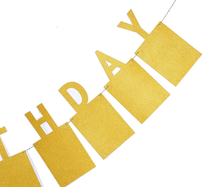 May include: Gold glitter Happy Birthday banner with each letter on a separate piece of cardstock. The banner is strung together with white string.