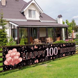 May include: A black banner with the words "Happy 100th Birthday" in rose gold lettering. The banner is decorated with rose gold balloons, confetti, and other celebratory graphics.