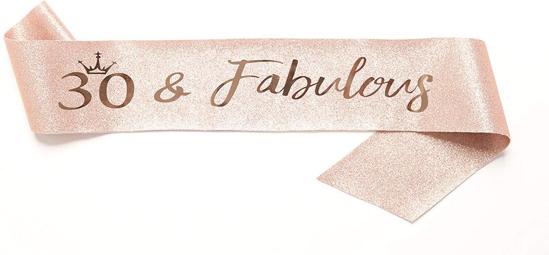 May include: A pink glitter sash with the text "30 & Fabulous" in gold lettering and a crown above the number 30.