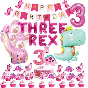 Peut inclure: D&eacute;corations de f&ecirc;te d'anniversaire sur le th&egrave;me des dinosaures roses et verts.  Comprend un ballon de dinosaure rose, un ballon de dinosaure vert, un ballon num&eacute;ro 3 rose, une banni&egrave;re rose et blanche qui dit "Joyeux anniversaire", et des cupcakes roses et blancs avec des d&eacute;corations de dinosaures.