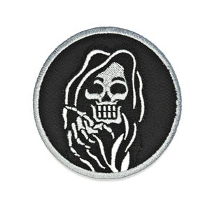 May include: Round black patch featuring a white Grim Reaper design. The reaper is depicted with a skull face, hooded robe, and skeletal hands. The patch has a silver border and is likely an iron-on or sew-on patch for clothing or accessories.