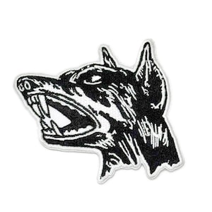May include: Black and white embroidered patch of a snarling dog's head. The dog has a fierce expression with bared teeth and a raised ear.