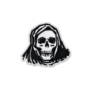May include: A black and white embroidered patch featuring a skull wearing a hooded cloak. The skull has dark eye sockets and a detailed jawline. The patch has a white border and is set against a white background.