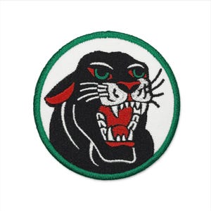 May include: Embroidered patch featuring a black panther with red accents and green eyes, set against a white background. The panther is roaring, with its mouth open, revealing white teeth and a red interior. The patch is circular, with a green border.