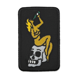 May include: Embroidered patch featuring a yellow figure reclining on a white skull, holding a green bottle. The patch has a black rectangular border. The design is a stylized illustration.