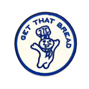 Può includere: Toppa ricamata con il personaggio di Pillsbury Doughboy in blu su sfondo bianco. Il testo "GET THAT BREAD" è in un bordo circolare blu attorno al personaggio. La toppa è rotonda e ha un bordo blu.