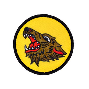 May include: A yellow embroidered patch with a black outline featuring a brown wolf with red teeth and tongue snarling.