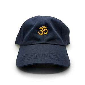 Puede incluir: Gorra de béisbol azul marino con un símbolo Om amarillo bordado en la parte delantera. La gorra tiene una visera curva y un diseño clásico de seis paneles. El sombrero está hecho de una tela duradera.