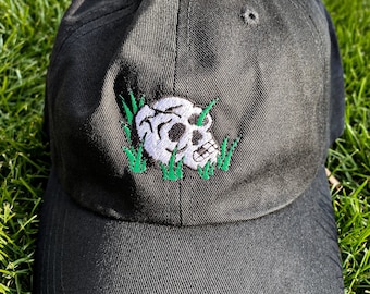 May include: A black baseball cap with a white skull and green grass embroidered on the front.