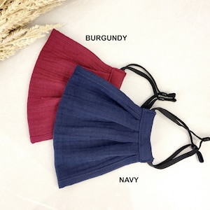 May include: Two face masks, one burgundy and one navy blue, with black elastic ear loops. The masks are made of a soft, textured fabric and have a pleated design.