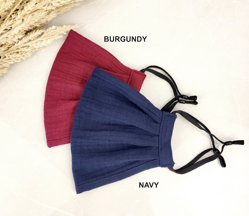 May include: Two face masks, one burgundy and one navy blue, with black elastic ear loops. The masks are made of a soft, textured fabric and have a pleated design.