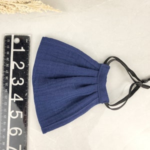 May include: A dark blue cotton face mask with black adjustable straps. The mask has pleats and is made of a soft, breathable fabric.