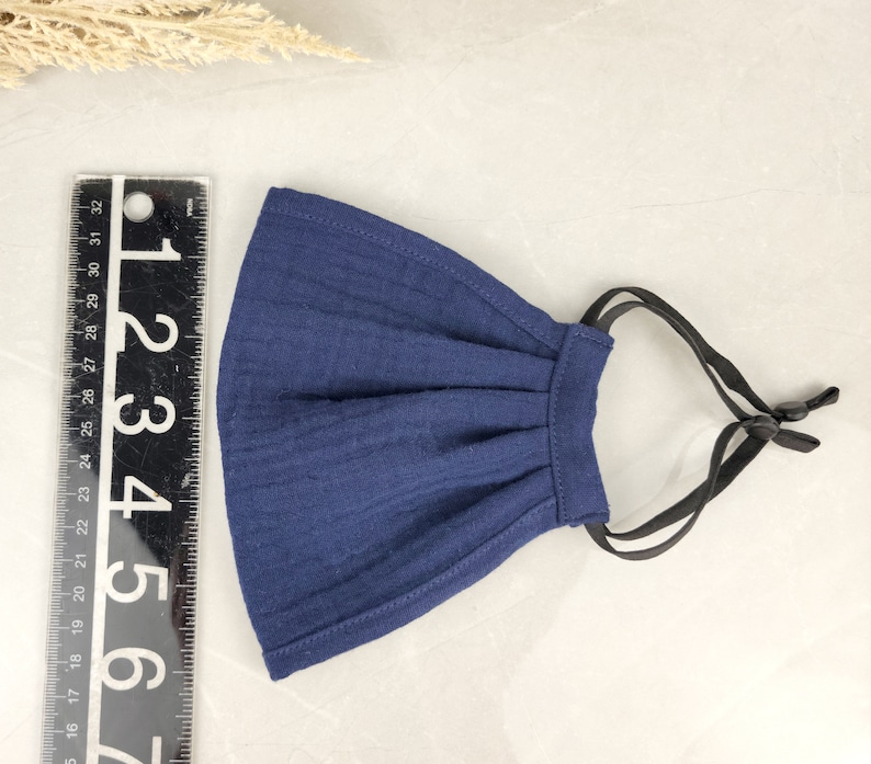 May include: A dark blue cotton face mask with black adjustable straps. The mask has pleats and is made of a soft, breathable fabric.