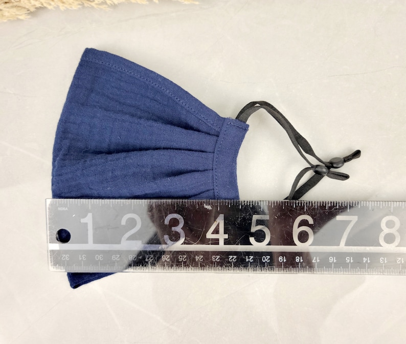 May include: A navy blue fabric face mask with adjustable ear loops. The mask is approximately 5 inches wide.