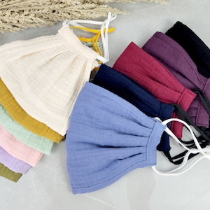 May include: A set of ten face masks in various colors, including beige, mustard yellow, light green, pink, lavender, olive green, light blue, navy blue, burgundy, and black. The masks are made of a soft, breathable fabric and have adjustable ear loops.