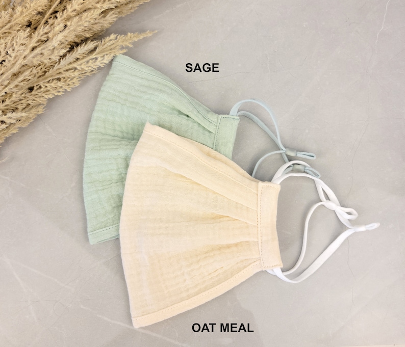 May include: Two face masks, one sage green and one oatmeal, with white elastic straps. The masks are made of a soft, breathable fabric.
