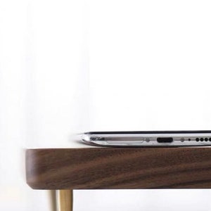 May include: A silver smartphone sits on a dark brown wooden table with gold metal legs.
