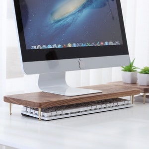 May include: A wooden computer monitor stand with a white keyboard resting on top. The stand has four gold metal legs and is made of dark wood.