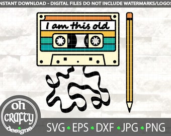 May include: A retro-style cassette tape with the text "I am this old" on it. The tape is yellow, blue, and green. A black and white pencil is next to the tape. The tape is on a white brick background.