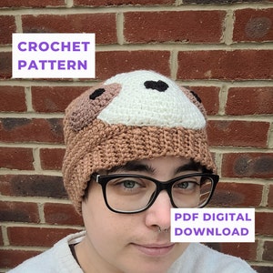May include: A crochet pattern for a brown and white sloth hat with black eyes. The pattern is available as a digital PDF download.