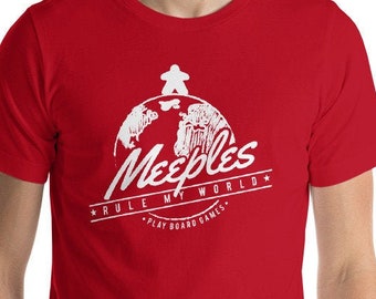 May include: Red short-sleeved t-shirt with a white graphic of a game piece standing on a globe with the text "Meeples Rule My World - Play Board Games".