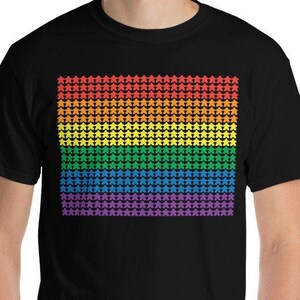 Peut inclure: Un t-shirt noir avec un motif d'étoiles arc-en-ciel. Les étoiles sont disposées en grille, chaque rangée représentant une couleur différente de l'arc-en-ciel.