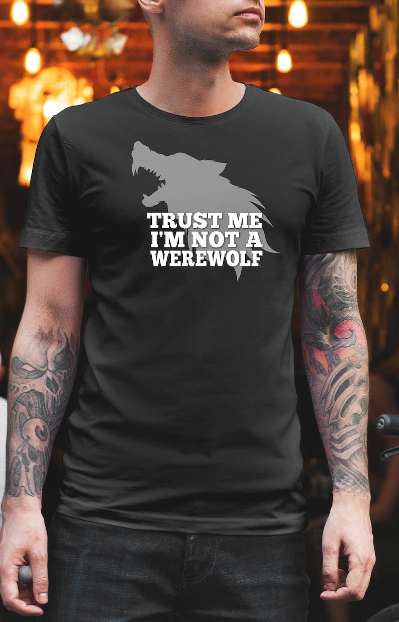 May include: Black t-shirt featuring a gray wolf head graphic and the text "TRUST ME I'M NOT A WEREWOLF" in white. The shirt is made of a soft material and is suitable for casual wear. The design is centered on the chest.