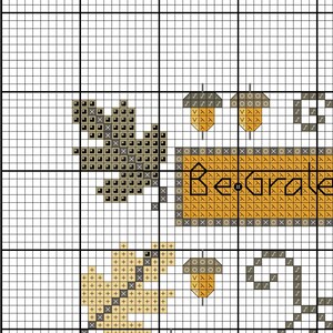 May include: Cross-stitch pattern featuring a squirrel, acorns, and the words "Be Grateful" in a rustic, fall-themed design. The design uses shades of brown, gold, and gray on a white background, perfect for autumn decor.
