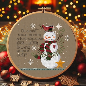 Può includere: Ricamo a punto croce in un telaio di legno raffigurante un pupazzo di neve con sciarpa rossa e verde, cappello nero e un cardinale. Il testo recita: "In una tranquilla mattina nevosa, un gentile pupazzo di neve aspettava di riscaldare l'inverno di qualcuno."