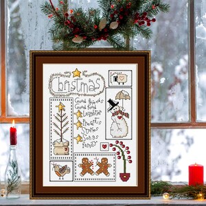 Può includere: Opera d'arte a punto croce incorniciata a tema natalizio. L'opera presenta la parola "Christmas" e vari elementi festivi come un pupazzo di neve, omini di pan di zenzero e un albero di Natale. La cornice è marrone e lo sfondo mostra una finestra innevata.