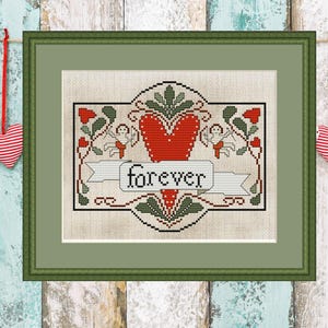 Può includere: Opera d'arte a punto croce incorniciata con un cuore rosso e la parola "forever" in uno stendardo. Il disegno comprende cherubini, foglie e bacche. Due cuori di stoffa sono appesi ai lati.