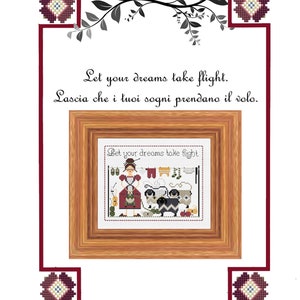Op de afbeelding: Borduurpatroon met een vrouw die was ophangt met de tekst "Let your dreams take flight." Het patroon is ingelijst in een houten lijst met een bordeauxrode rand. De tekst "Lascia che i tuoi sogni prendano il volo." staat onder de lijst.